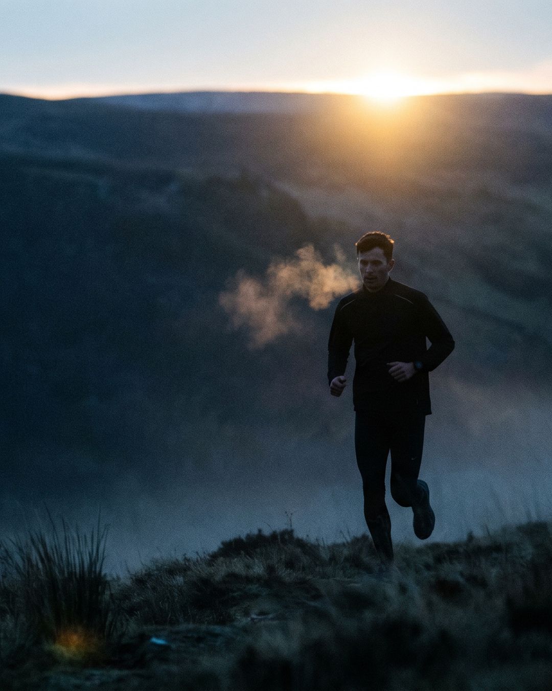 A runner on a misty hillside at sunrise.